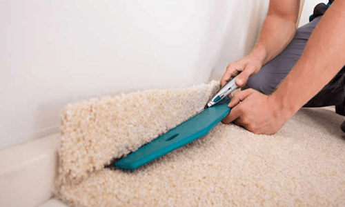 Worker cutting carpet edge with tool.