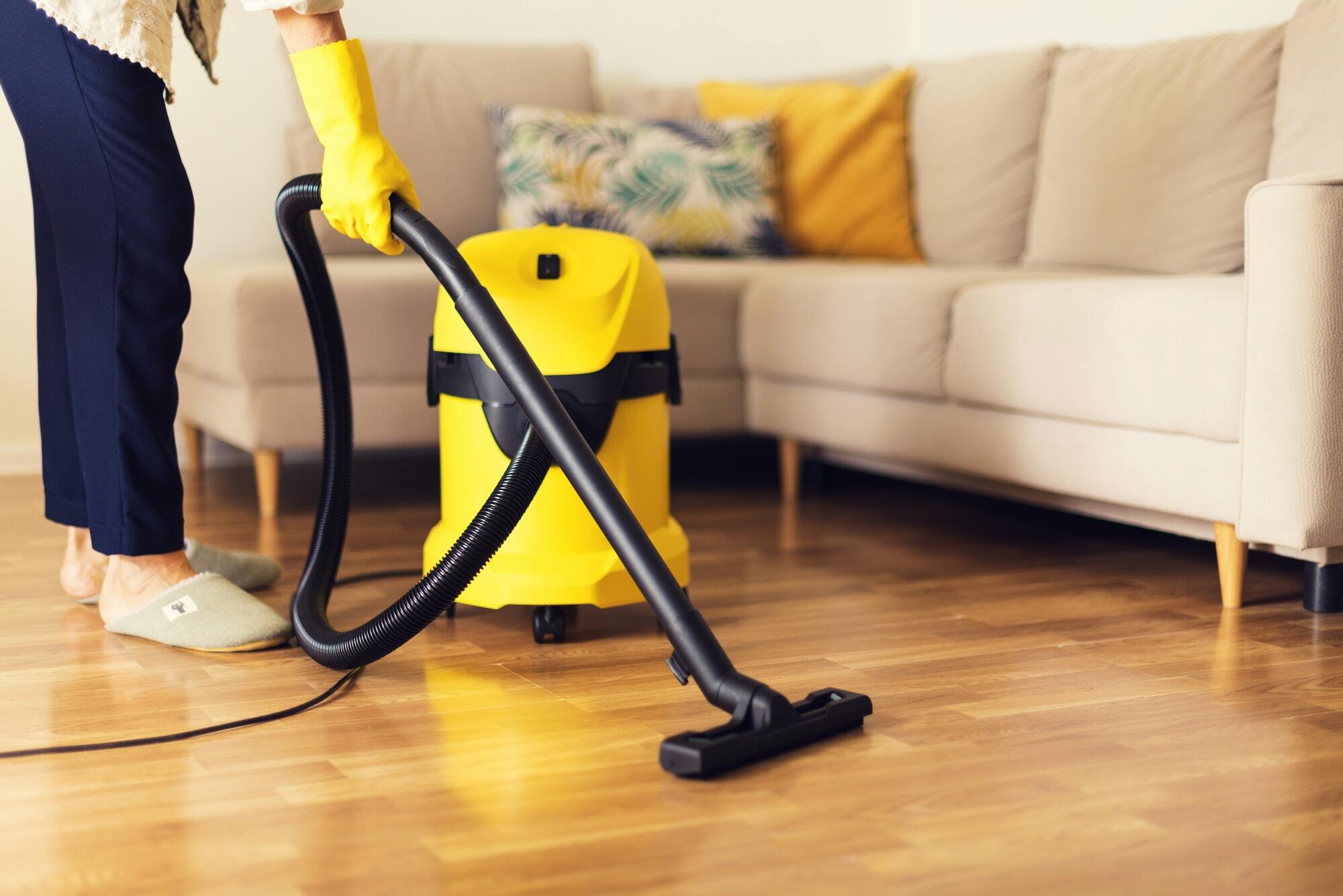 Vacuuming sofa with yellow cleaner in bright living room