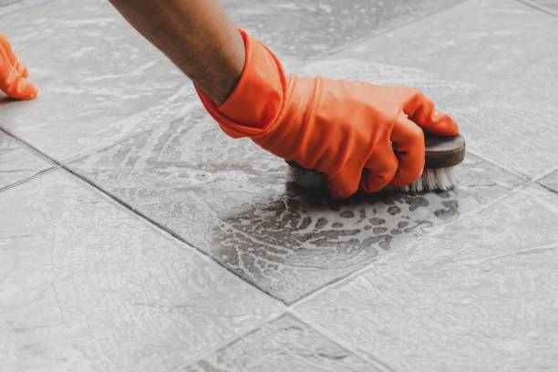 Person scrubbing tile floor with brush and gloves.