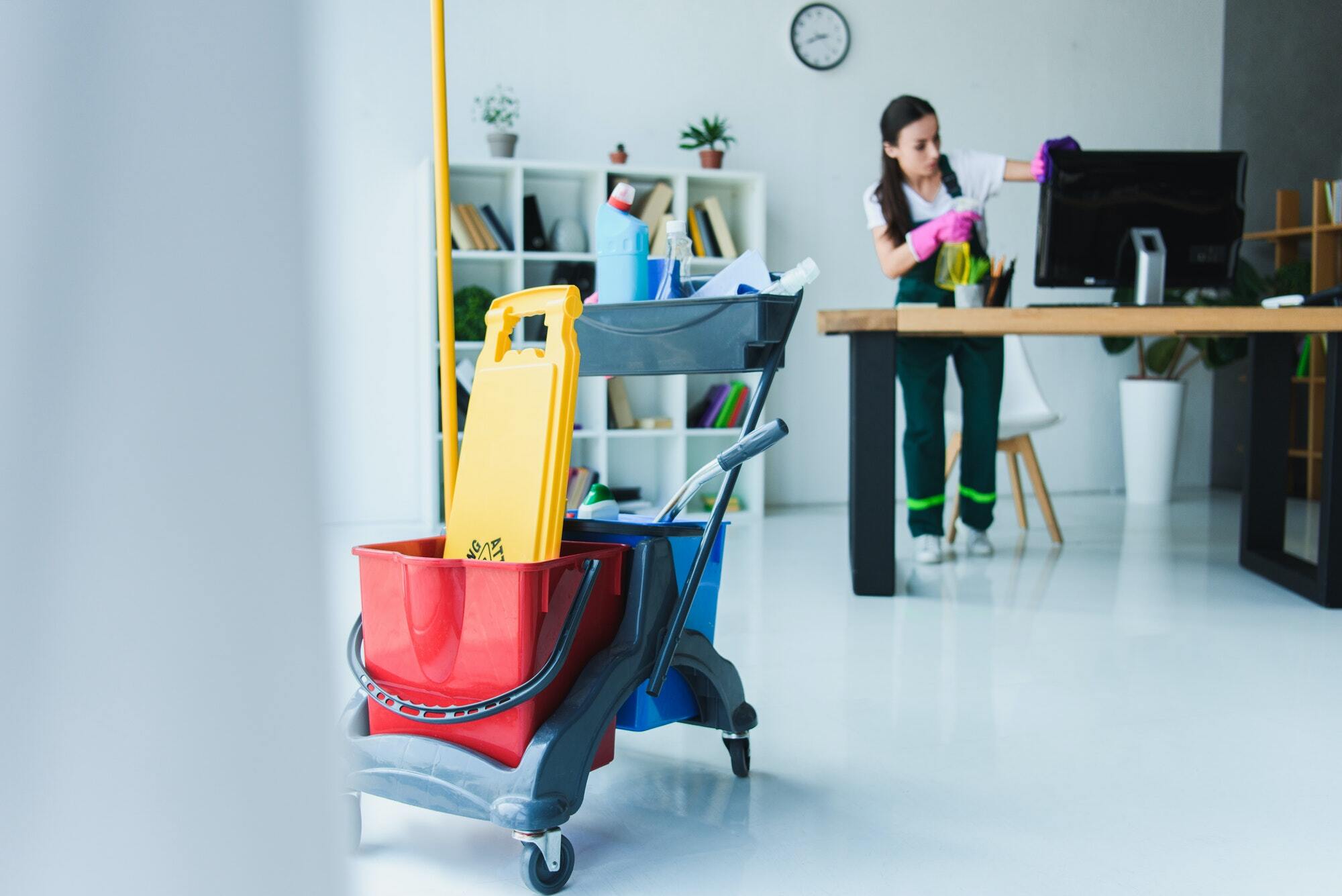 Young female janitor cleaning office with equipment